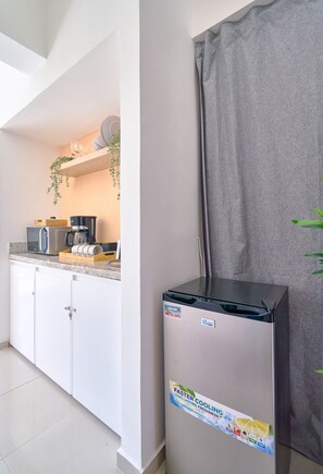 Eine Küche mit weißen Schränken, einer Mikrowelle, einer Kaffeemaschine und einem Kühlschrank mit einem Aufkleber.