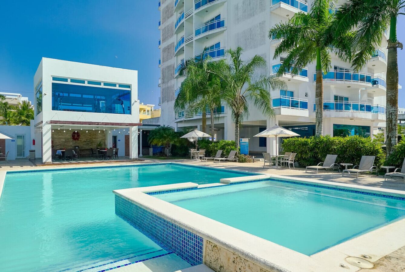Un hotel con piscina, sillones de descanso y palmeras.