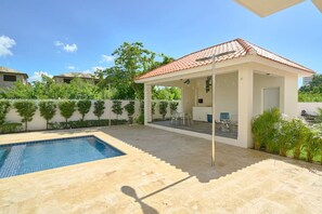 A covered outdoor area with a pool, seating, and a white building with a red roof. - BeachsideGetaway|3BR|Pool|5Min walk to Beach|Wi-Fi (Juan Dolio)