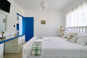 A bedroom with a bed, a desk, a blue door, a window with curtains, and a hanging light fixture. - BeachsideGetaway|3BR|Pool|5Min walk to Beach|Wi-Fi (Juan Dolio)
