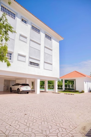 A white building with a tiled driveway and a parked car. - BeachsideGetaway|3BR|Pool|5Min walk to Beach|Wi-Fi (Juan Dolio)