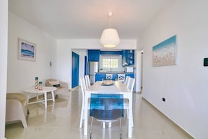 A modern kitchen with blue cabinets, a dining area with a white table and chairs, and a large window. - BeachsideGetaway|3BR|Pool|5Min walk to Beach|Wi-Fi (Juan Dolio)