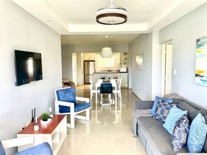 A modern living room with a sofa, chairs, a dining table, and a kitchen in the background. - BeachsideGetaway|3BR|Pool|5Min walk to Beach|Wi-Fi (Juan Dolio)