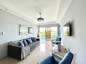 A modern living room with a sofa, a dining table, and a TV mounted on the wall. - BeachsideGetaway|3BR|Pool|5Min walk to Beach|Wi-Fi (Juan Dolio)