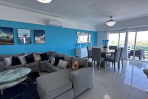 A modern living room with a sectional sofa, a dining area with a chandelier, and artwork on the walls. - BeachSide Blue Cleef Playa Juan Dolio Las Velas (Juan Dolio)
