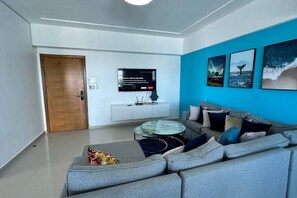 Ein modernes Wohnzimmer mit einem grauen Sofa, einem Glastisch und einem flachbildfernseher an der Wand.