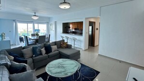 En moderne stue med en grå hjørnesofa, et marmorbord og et spiseområde med et hvidt bord og stole.