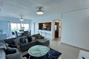 A modern living room with a grey sectional sofa, a marble coffee table, and a dining area with a white table and chairs. - BeachSide Blue Cleef Playa Juan Dolio Las Velas (Juan Dolio)