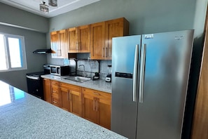 A kitchen with wooden cabinets, a stainless steel refrigerator, a microwave, and a sink. - BeachSide Blue Cleef Playa Juan Dolio Las Velas (Juan Dolio)