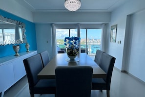 A dining area with a table, chairs, a chandelier, and a view through large windows. - BeachSide Blue Cleef Playa Juan Dolio Las Velas (Juan Dolio)