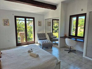 A hotel room with a bed, a desk, a chair, and a balcony with a view of greenery. - Les Palmiers de Beauvallon House, rated 5 stars, sleeps 6, with a pool (Grimaud)