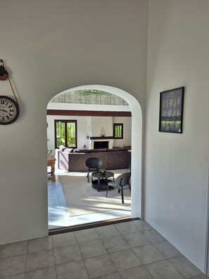 Vista interna de um quarto com piso de azulejos, um sofá, uma mesa e cadeiras.