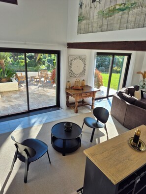 A spacious living area with a large sliding glass door leading to an outdoor patio, a wooden dining table, and a comfortable seating arrangement. - Les Palmiers de Beauvallon House, rated 5 stars, sleeps 6, with a pool (Grimaud)