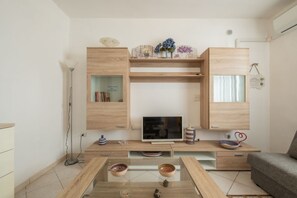 Un soggiorno moderno con televisione a schermo piatto, mobili contenitori in legno e un tavolino da caffè in vetro.