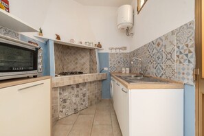 A compact kitchen with a microwave, stove, sink, and patterned tiles. - A Cà du Peppino | Your Retreat in the Heart of CalasettaDiscover the authentic charm of Sardinia by staying at A Cà du Peppino, a welcoming apartment located in the center of Calasetta, just 200 meters from the tourist harbor, the town’s best restaur (Calasetta)