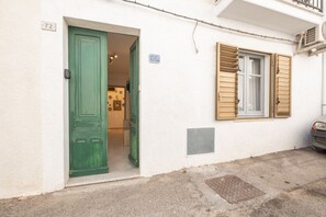 A building entrance with a green door, a window with shutters, and a small sign above the door. - A Cà du Peppino | Your Retreat in the Heart of CalasettaDiscover the authentic charm of Sardinia by staying at A Cà du Peppino, a welcoming apartment located in the center of Calasetta, just 200 meters from the tourist harbor, the town’s best restaur (Calasetta)