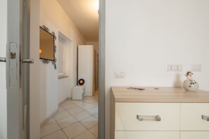 A hallway with a door, a mirror, a small table with a decorative item, and a light switch. - A Cà du Peppino | Your Retreat in the Heart of CalasettaDiscover the authentic charm of Sardinia by staying at A Cà du Peppino, a welcoming apartment located in the center of Calasetta, just 200 meters from the tourist harbor, the town’s best restaur (Calasetta)