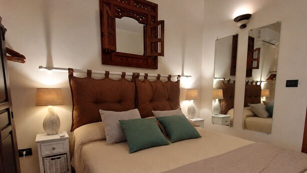 Una camera da letto con un letto grande, due comodini, un tavolino e uno specchio, con un punto luce fissato al muro.
