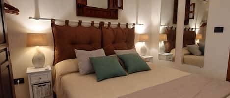 Une chambre à coucher avec un grand lit, deux tables de chevet, une commode, un miroir et un luminaire fixé au mur.