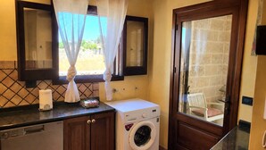 Una cucina funzionale con lavatrice, una finestra con tende e un'uscita verso uno spazio esterno.