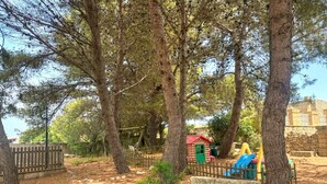 Un'area giochi con alberi, una recinzione in legno e un piccolo edificio con tetto rosso.
