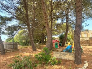 Ein Spielplatz mit Bäumen, einem Holzzaun und einem kleinen Gebäude mit rotem Dach.
