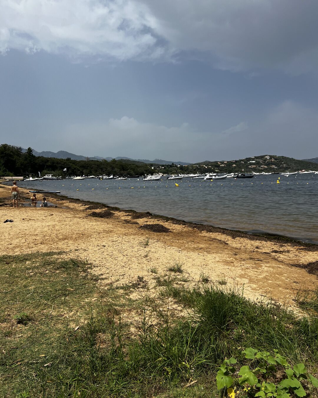 A beach with boats, a sandy shore, and a hilly landscape in the background.