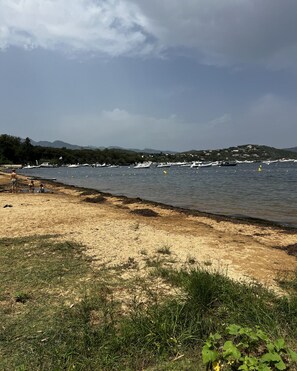 A beach with boats, a sandy shore, and a hilly landscape in the background. - New bungalow at a 3-star campground—right on the water (Porto-Vecchio)