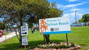 A welcome sign for Sylvan Beach with a one-way direction sign and a speed limit sign.