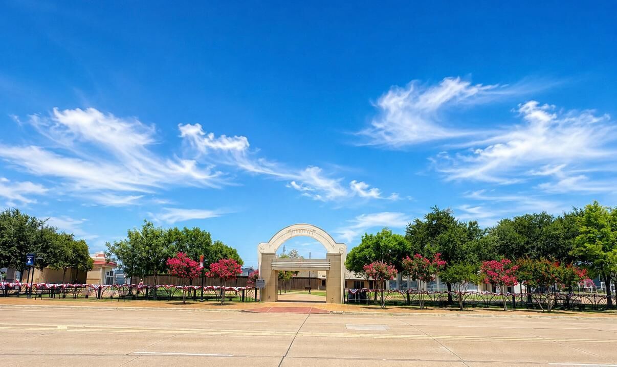 An entrance with a clear sky, a paved area, and trees with pink flowers.