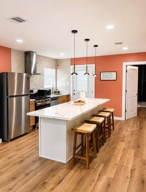 A modern kitchen with a central island, stainless steel appliances, and wooden bar stools.