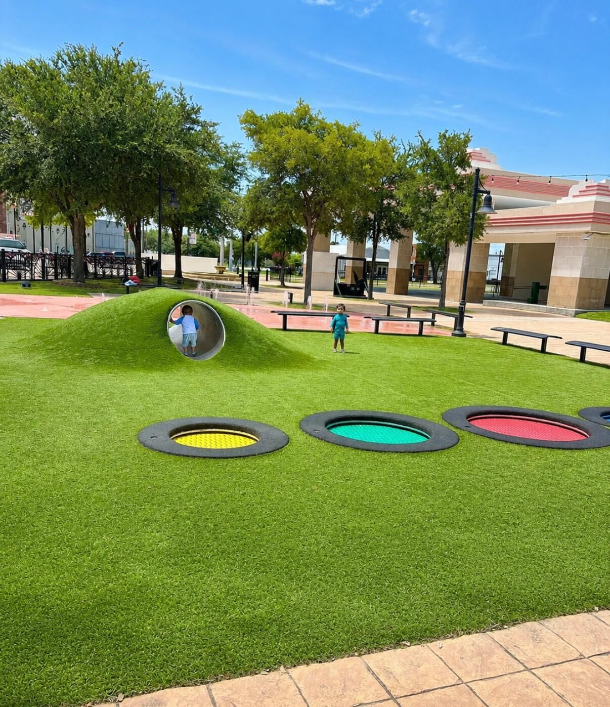 Un parc infantil amb tobogan i zones de jocs circulars sobre un camp de gespa.