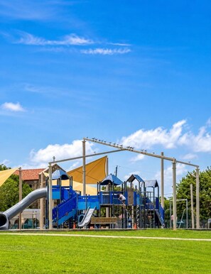 A playground with slides and climbing structures, surrounded by a grassy area and a clear sky. - Home: 3 Minutes to Sylvan Beach with a Hot Tub and Office Space (La Porte)