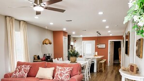 A living room with a red sofa, a dining area with a table and chairs, a ceiling fan, and a white console table with decorative items.