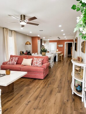 A living room with a red sofa, a dining area with a table and chairs, a ceiling fan, and a white console table with decorative items.