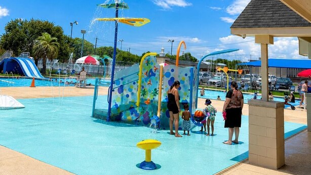 A swimming pool area with a water play structure, a covered seating area, and a clear blue sky.