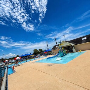 An outdoor swimming pool area with a clear sky, a covered seating area, and a building in the background. - Home: 3 Minutes to Sylvan Beach with a Hot Tub and Office Space (La Porte)