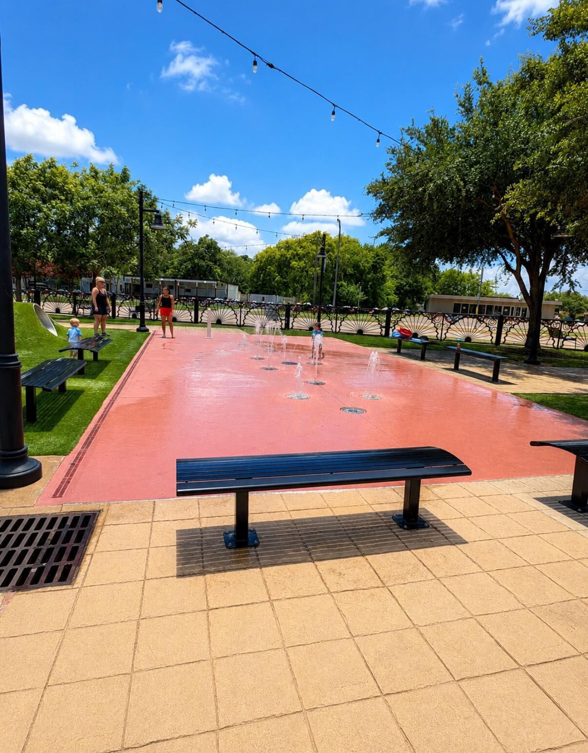 Un parc avec une aire de jeux rouge, des bancs et une fontaine.