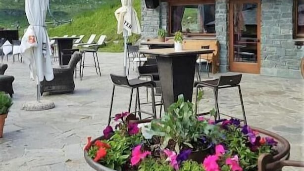 A wooden building with balconies, outdoor seating, and a mountainous backdrop. - Hotel Mon Reve (Valtournenche)