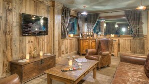 A rustic interior with wooden walls, a flat-screen TV, leather furniture, and a dining table with candles. - Hotel Mon Reve (Valtournenche)