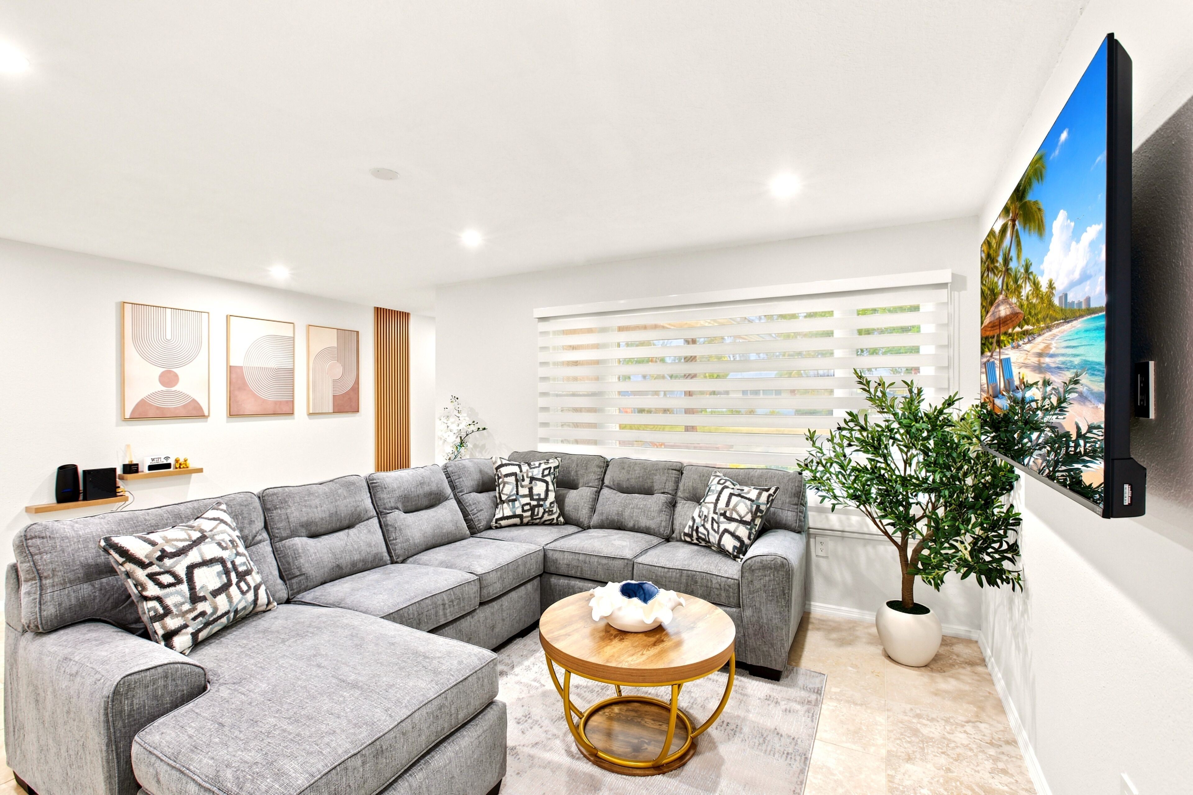 A modern living room with a sectional sofa, a round coffee table, and a large flat-screen TV mounted on the wall.