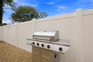 A stainless steel outdoor grill with four burners and a side shelf, set against a white fence and a clear sky. - Heated Saltwater Pool, Game Room&Mini Golf. Near Anna Maria Island & IMG Academy (Bradenton)