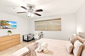 A bedroom with a bed, a desk, a chair, a ceiling fan, a window with blinds, and a painting of a beach scene. - Heated Saltwater Pool, Game Room&Mini Golf. Near Anna Maria Island & IMG Academy (Bradenton)