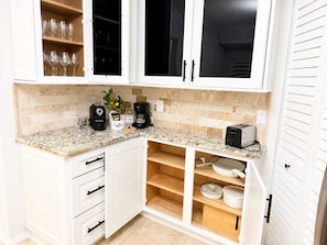 Eine Küche mit weißen Schränken, einer Kaffeemaschine, einem Toaster und einem Regal mit Gläsern.