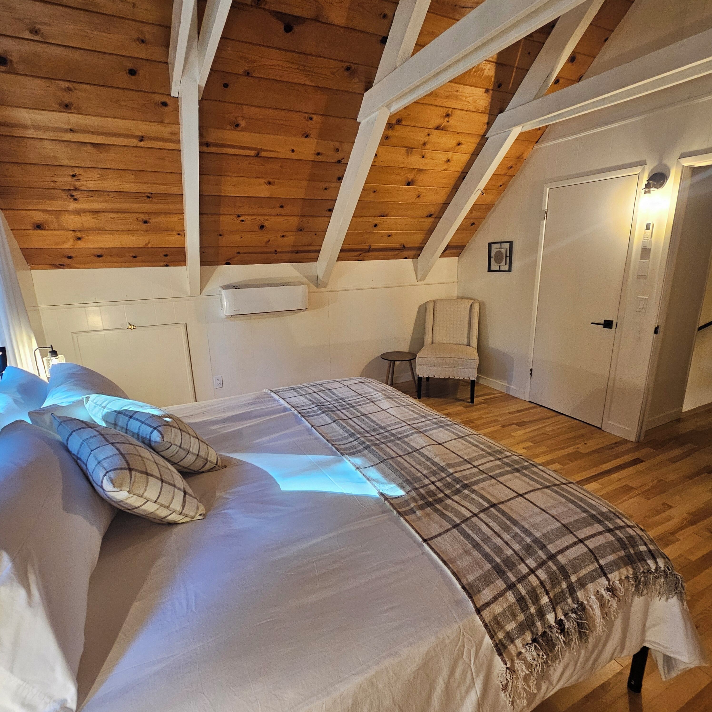 Un dormitorio con techo de madera, una cama con manta escocesa, una silla y una puerta.