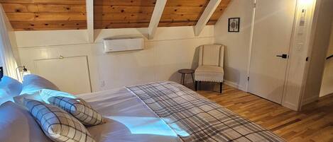 Un dormitorio con techo de madera, una cama con manta escocesa, una silla y una puerta.