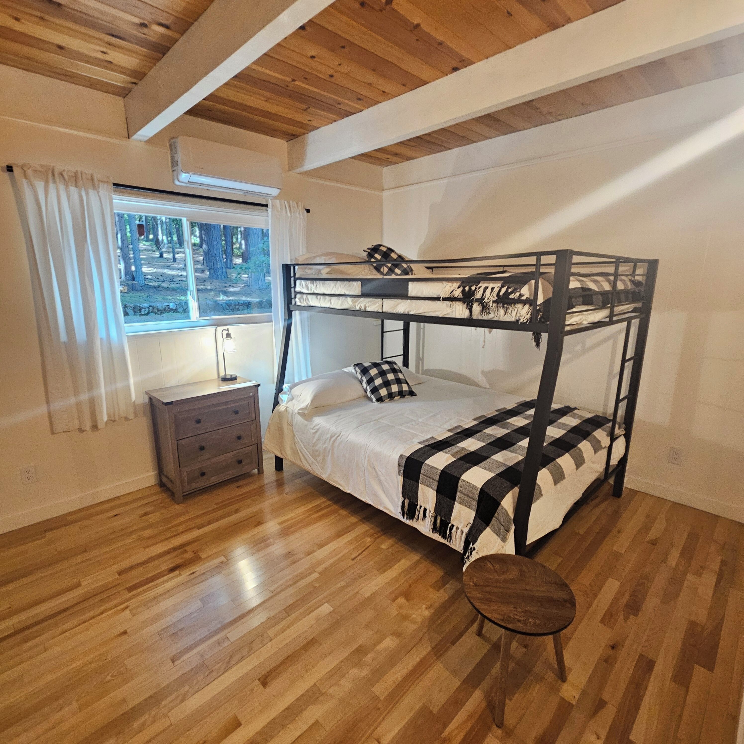 A bunk bed with a checkered blanket, a bedside table, a lamp, and a window with curtains.