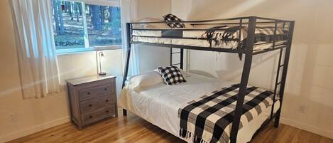 A bunk bed with a checkered blanket, a bedside table, a lamp, and a window with curtains.