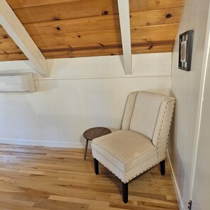 Ein Zimmer mit Holzboden, einem gemusterten Sessel, einem kleinen runden Tisch und einer weißen Wand mit einem gerahmten Bild.