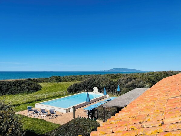 Piscina con vistas al mar, rodeada de vegetación y un cielo despejado.